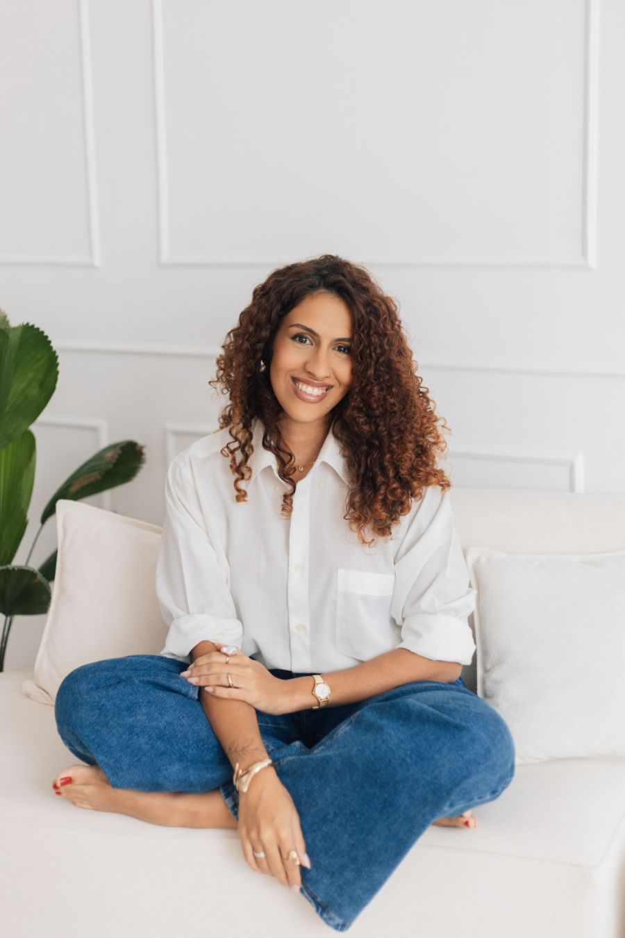 Aline Valente sentada no sofá de pernas cruzadas, sorrindo