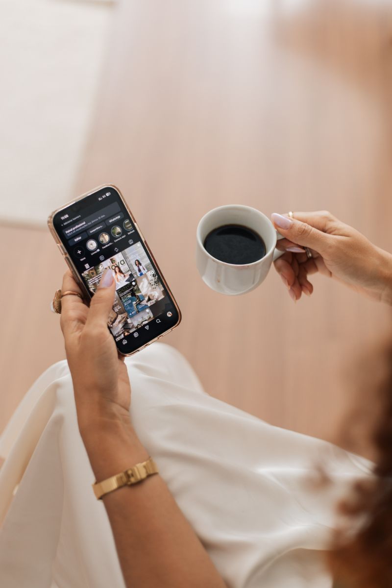 Mãos segurando o celular e uma xícara de café