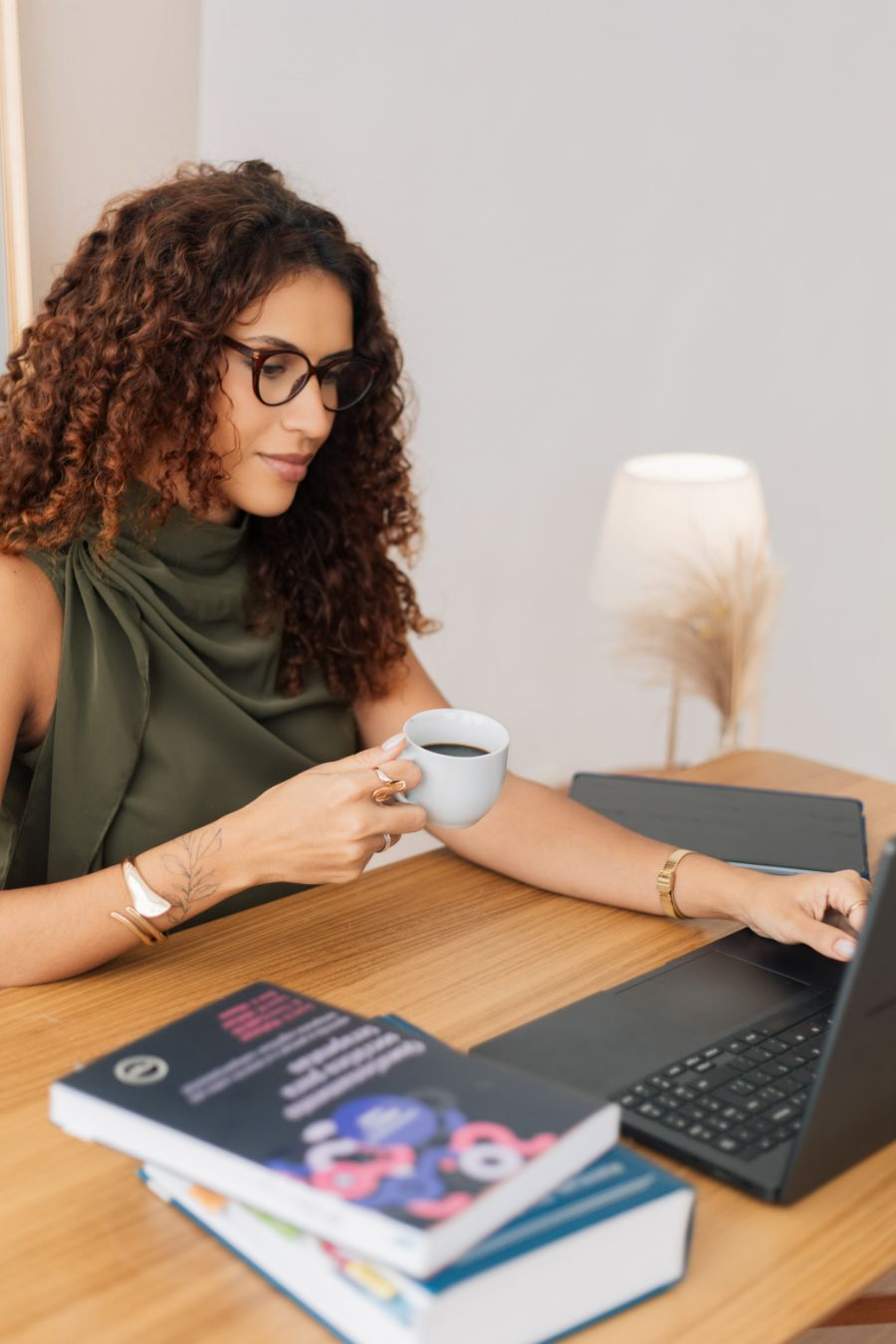 Aline Valente de óculos, à mesa com café, notebook e livros de TCC e Terapia do Esquema